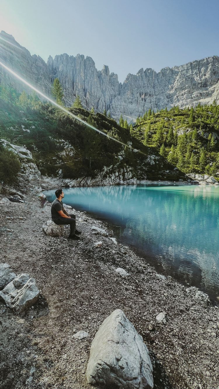 lago azul turquesa y persona sentado en una roca mirando hacia el lago sorapis